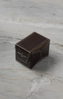 A three-quarter high-angle shot of the official folding dark brown textured leather watch travel case resting closed on a light grey marble surface