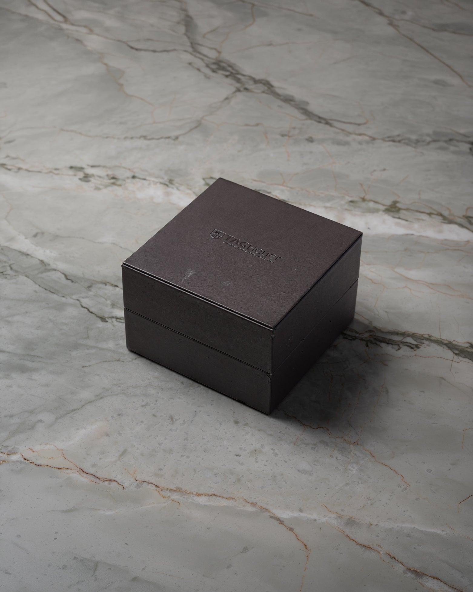 angled overview of the closed, textured black TAG Heuer luxury watch presentation box sitting on a stone studio surface