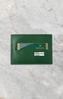 Official green Rolex international guarantee warranty card resting inside its classic green leather document wallet sleeve on a marble surface