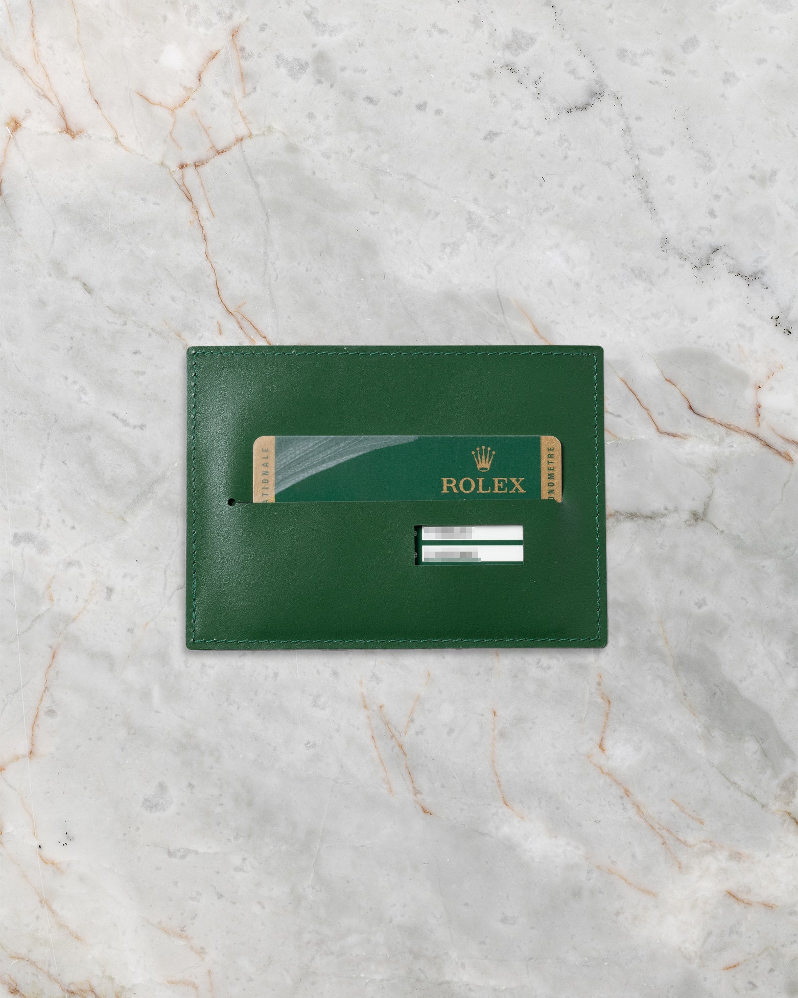 Official green Rolex international guarantee warranty card resting inside its classic green leather document wallet sleeve on a marble surface