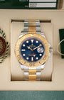 direct frontal portrait of the 2010 two-tone Rolex Yacht-Master 16623 watch with a royal blue dial resting inside its green presentation box wrapper