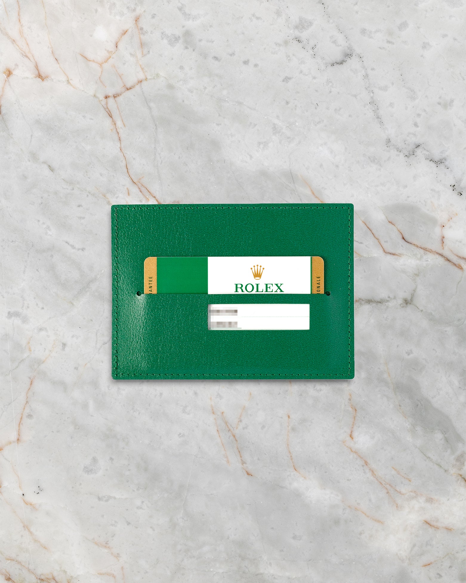 Official green Rolex international guarantee warranty card for a pre-owned 2016 Rolex Datejust II reference 116300 resting inside its leather wallet on marble