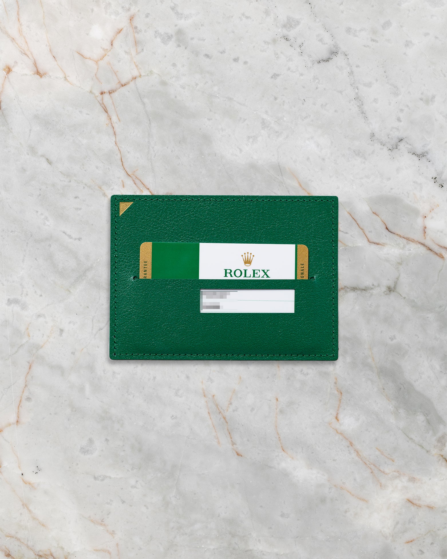 Official green Rolex international guarantee warranty card resting inside its classic green leather document wallet sleeve on marble