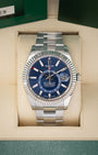 A front studio portrait of the 2023 Rolex Sky-Dweller 336934 watch featuring a bright blue dial and steel Oyster bracelet inside its green presentation box wrapper