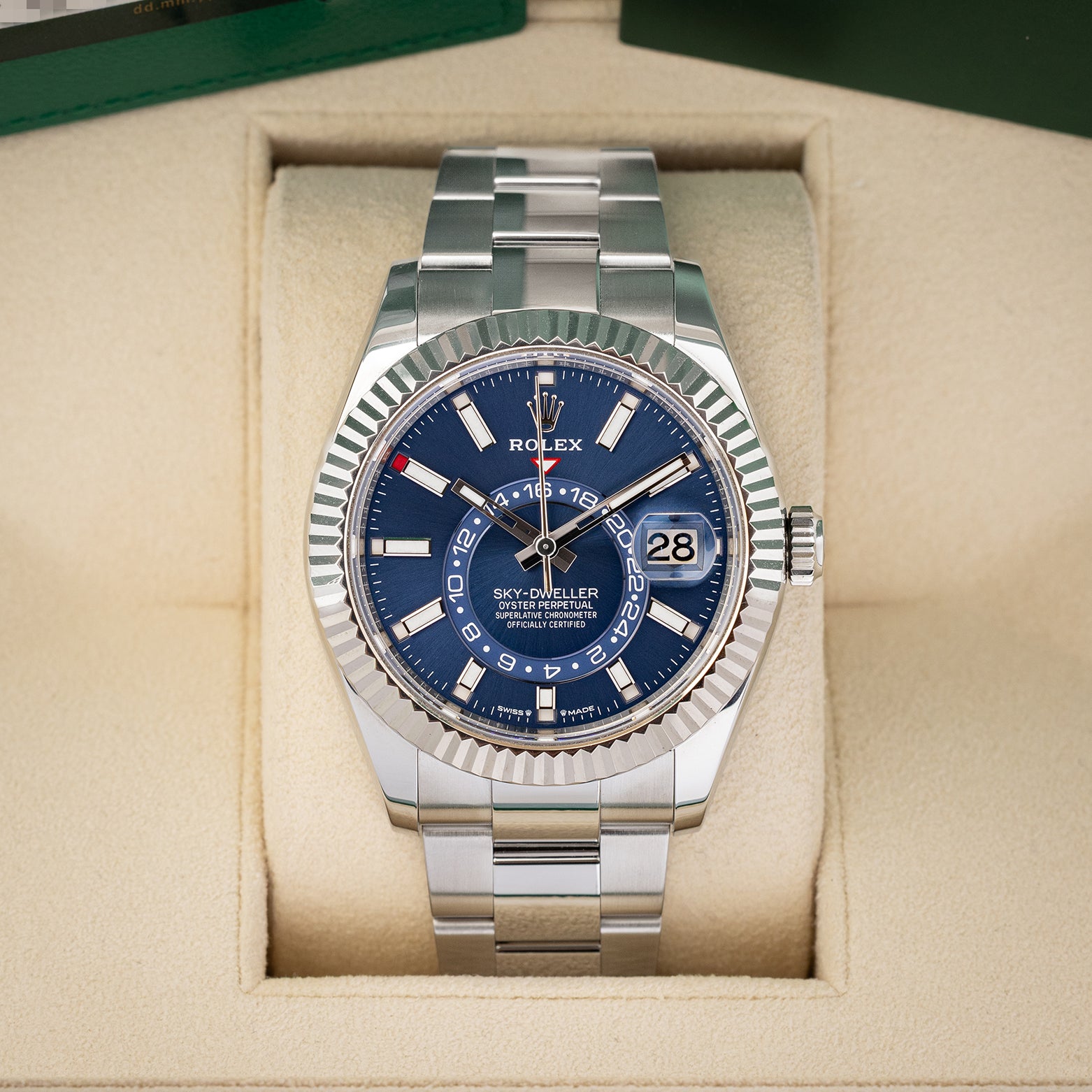 A front studio portrait of the 2023 Rolex Sky-Dweller 336934 watch featuring a bright blue dial and steel Oyster bracelet inside its green presentation box wrapper