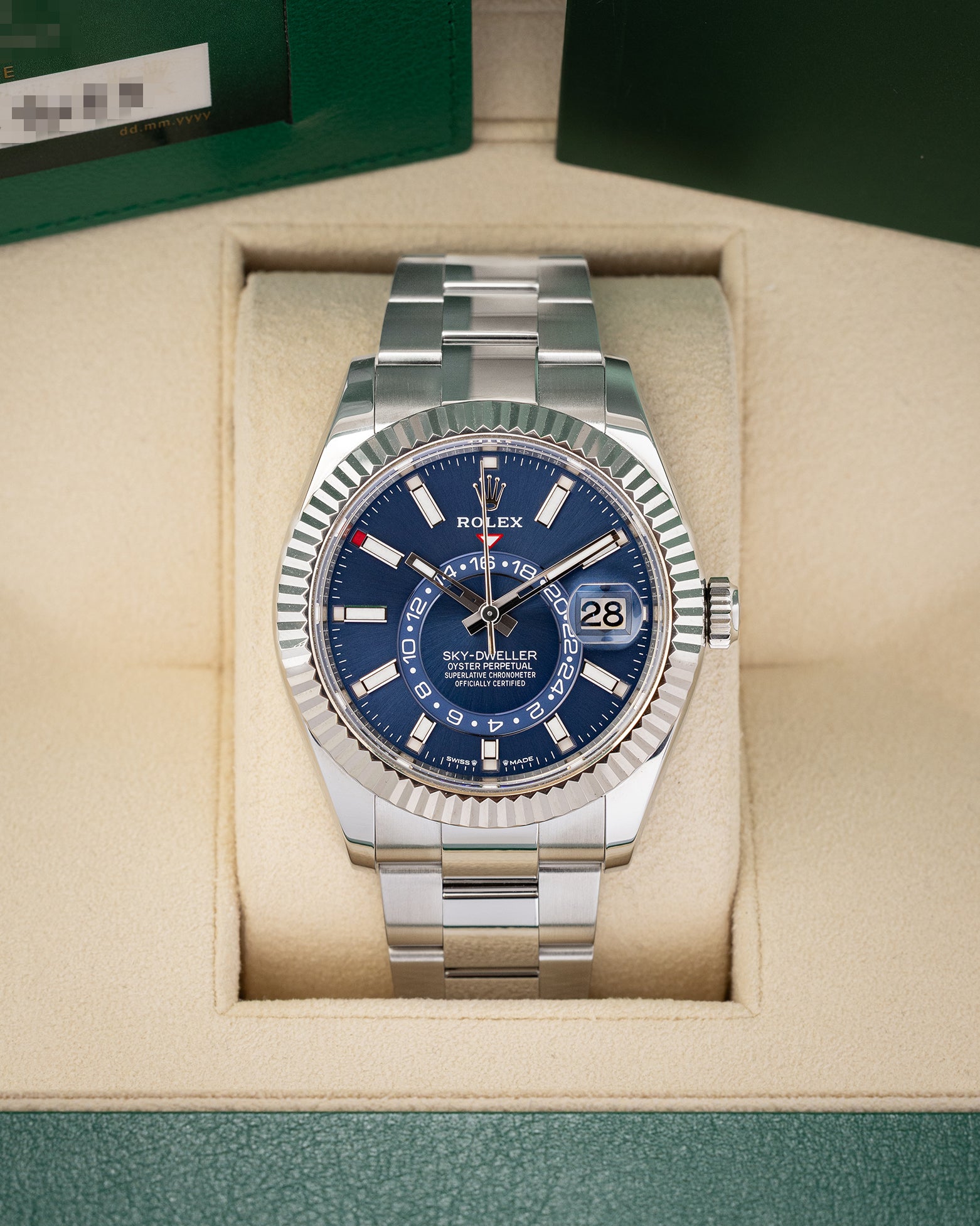 A front studio portrait of the 2023 Rolex Sky-Dweller 336934 watch featuring a bright blue dial and steel Oyster bracelet inside its green presentation box wrapper