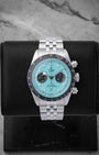 2025 Tudor Black Bay Chrono 79360N-0024 featuring a vibrant flamingo blue turquoise dial on a black studio display stand