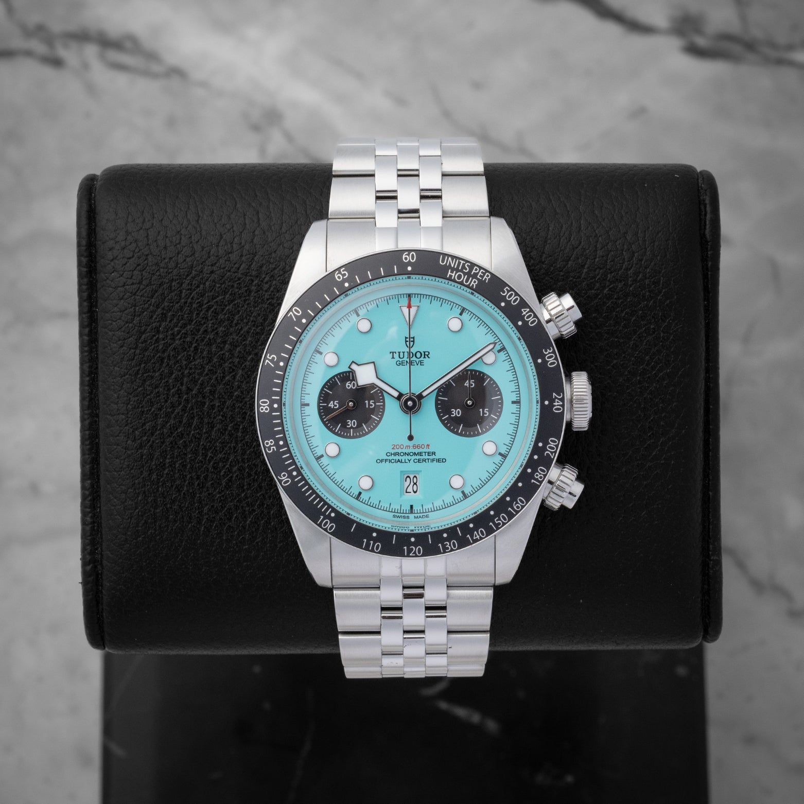 2025 Tudor Black Bay Chrono 79360N-0024 featuring a vibrant flamingo blue turquoise dial on a black studio display stand