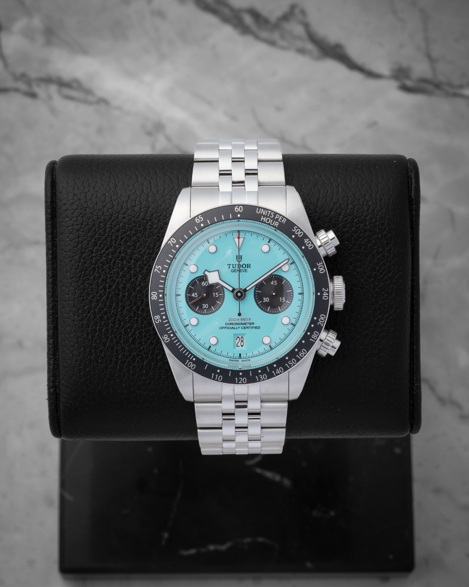 2025 Tudor Black Bay Chrono 79360N-0024 featuring a vibrant flamingo blue turquoise dial on a black studio display stand