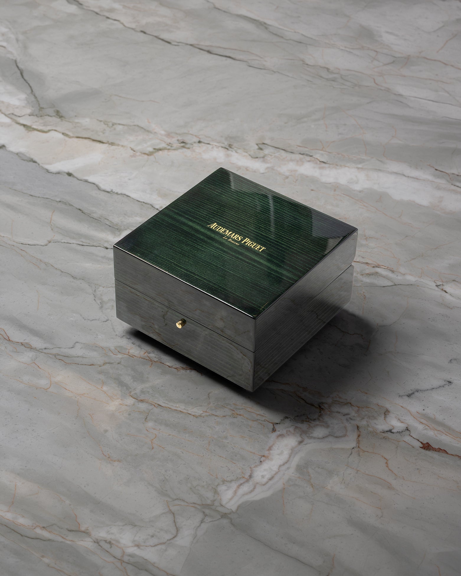 angled overview of the closed, high-gloss green lacquered wooden Audemars Piguet luxury watch box sitting on a stone studio surface.