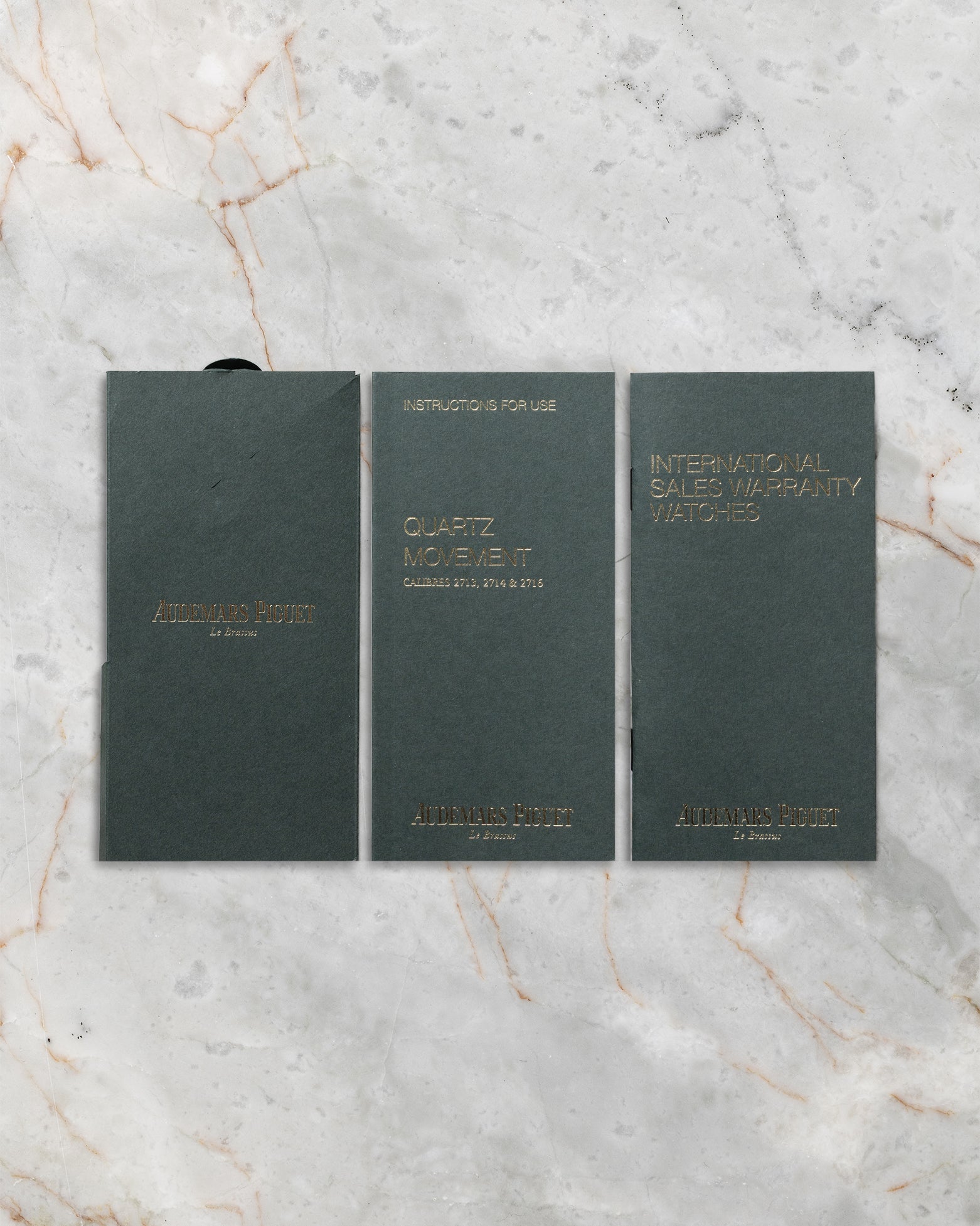 flat-lay view of the three official dark green Audemars Piguet warranty certificates, user manual booklets, and service guides resting on marble