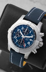 Angled front view of a preowned Breitling Avenger Chronograph GMT A24315101C1X1 featuring a blue stencil dial, red GMT hand, and blue leather strap with white stitching