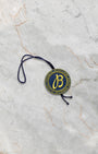 The official circular gold and blue Breitling Certified Chronometer hang tag with cord laid flat on a marble background