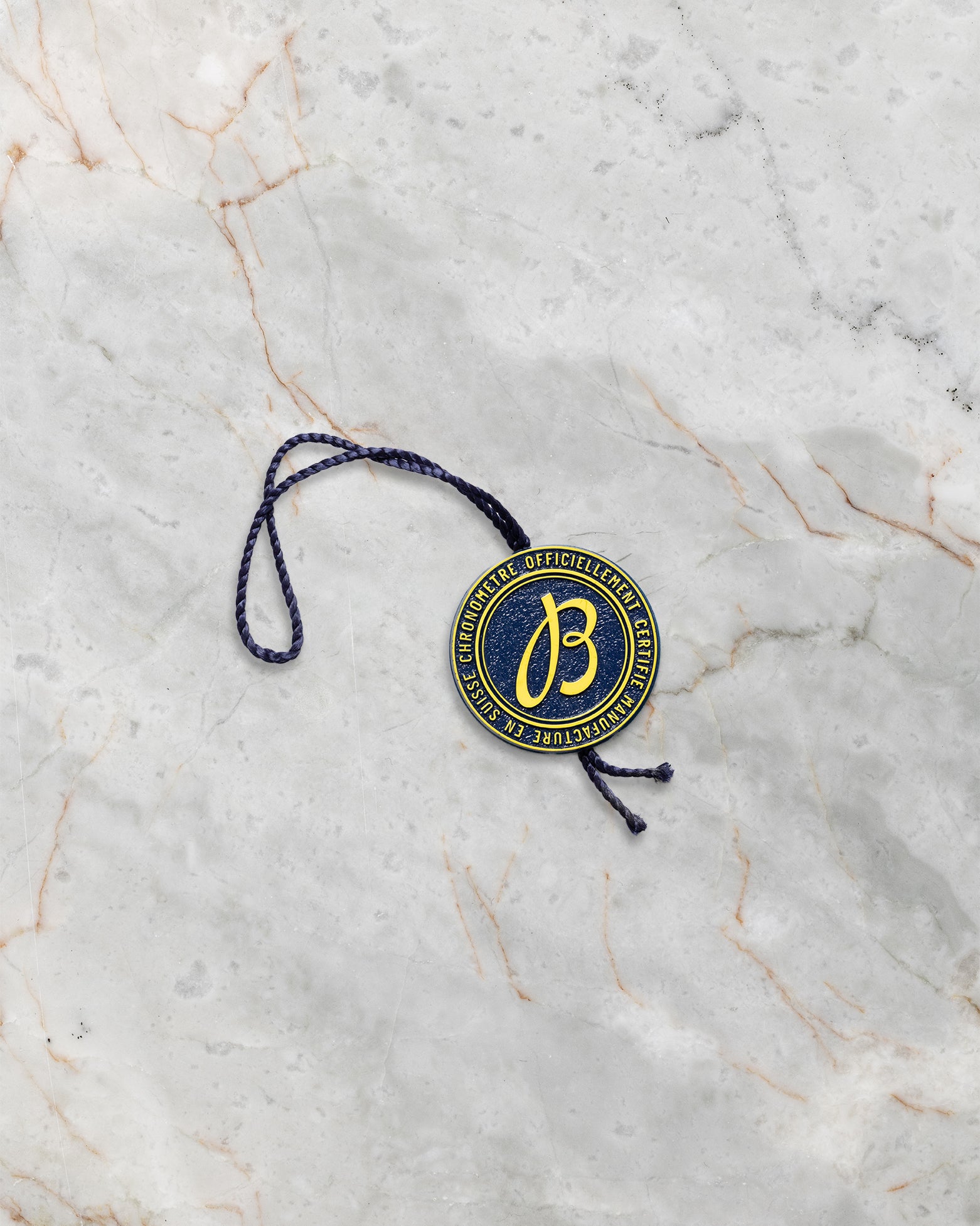 The official circular gold and blue Breitling Certified Chronometer hang tag with cord laid flat on a marble background