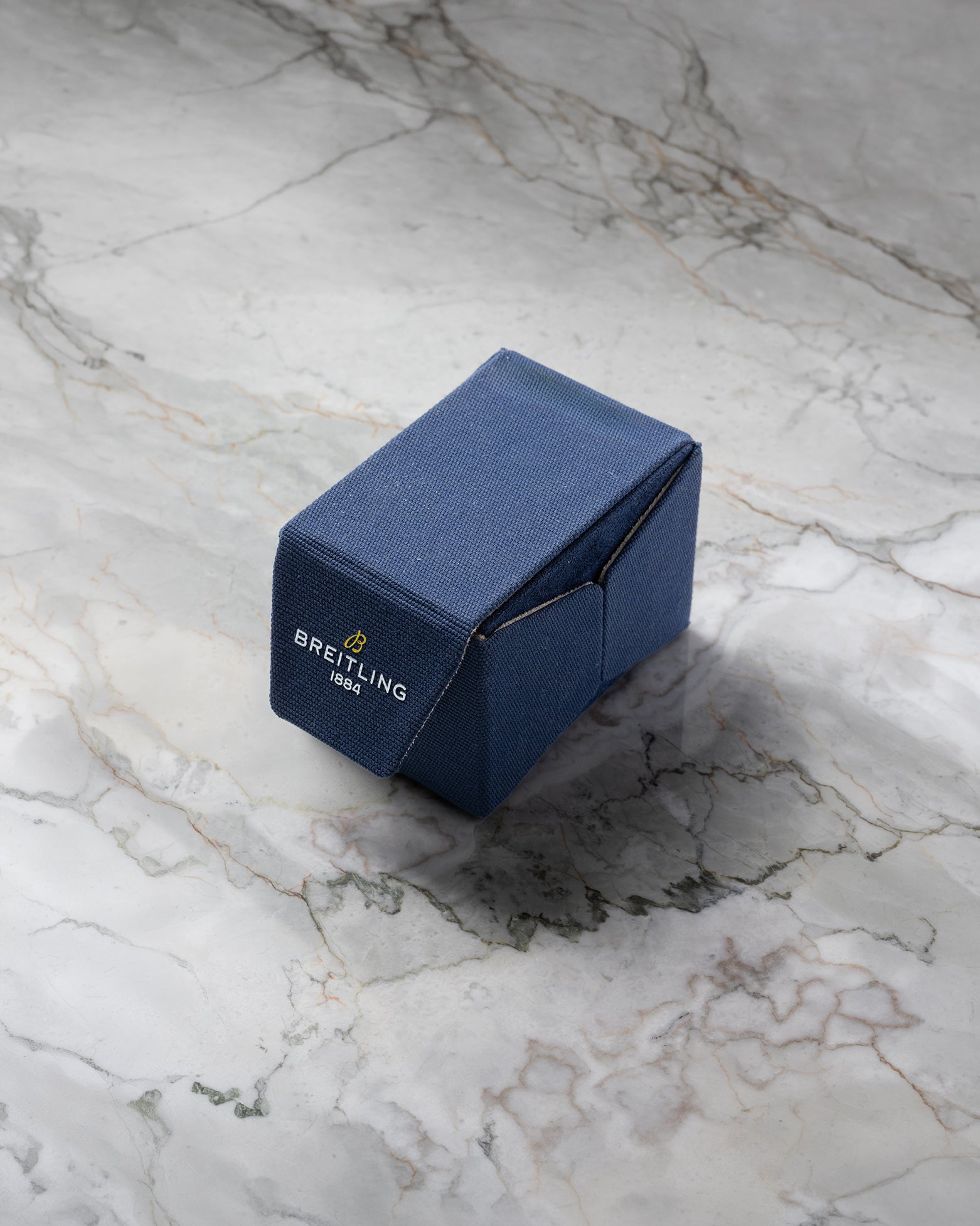 A clsoed blue Breitling sustainable fabric watch presentation travel box sitting on a textured grey marble background