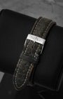 Close-up view of the premium dark grey textured exotic leather strap on a watch cushion, focusing on the polished stainless steel pin buckle clasp engraved with the classic Breitling script logo