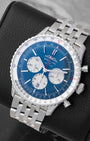 An angled studio profile view of a 43mm stainless steel Breitling Navitimer B01 automatic watch on a leather cushion