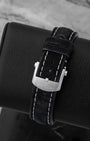 Rear view of the black leather watch strap secured by a polished stainless steel pin tang buckle clasp engraved with the Breitling brand emblem