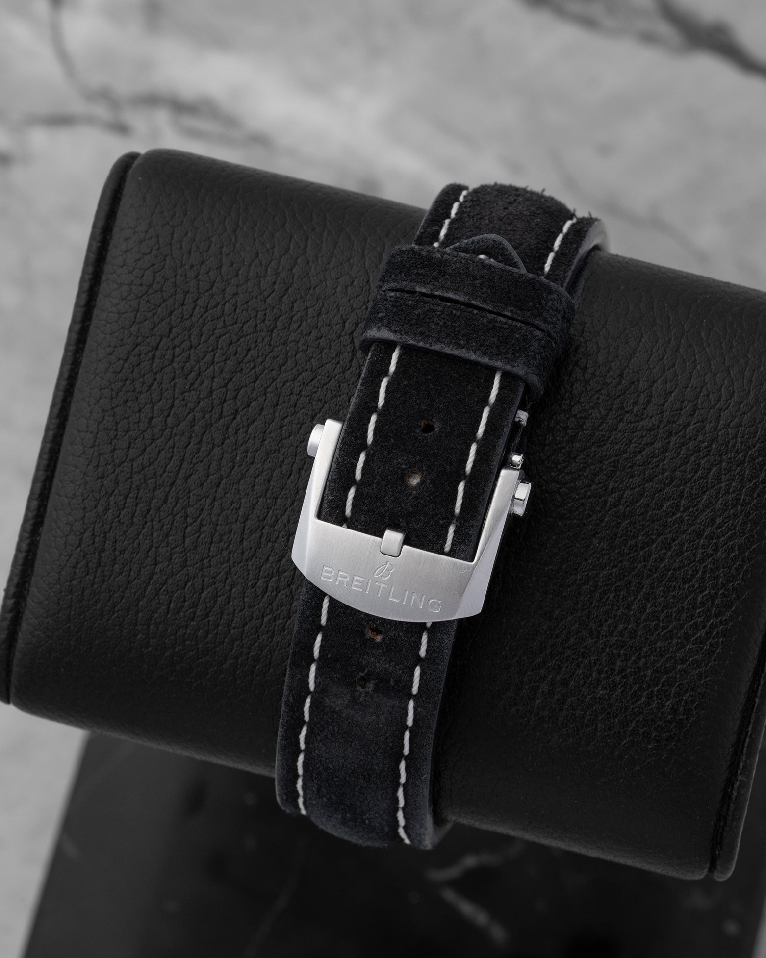 Rear view of the black leather watch strap secured by a polished stainless steel pin tang buckle clasp engraved with the Breitling brand emblem
