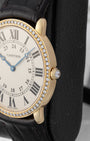 Close-up side profile of the yellow gold watch case highlighting the circular-grained crown set with a diamond cabochon