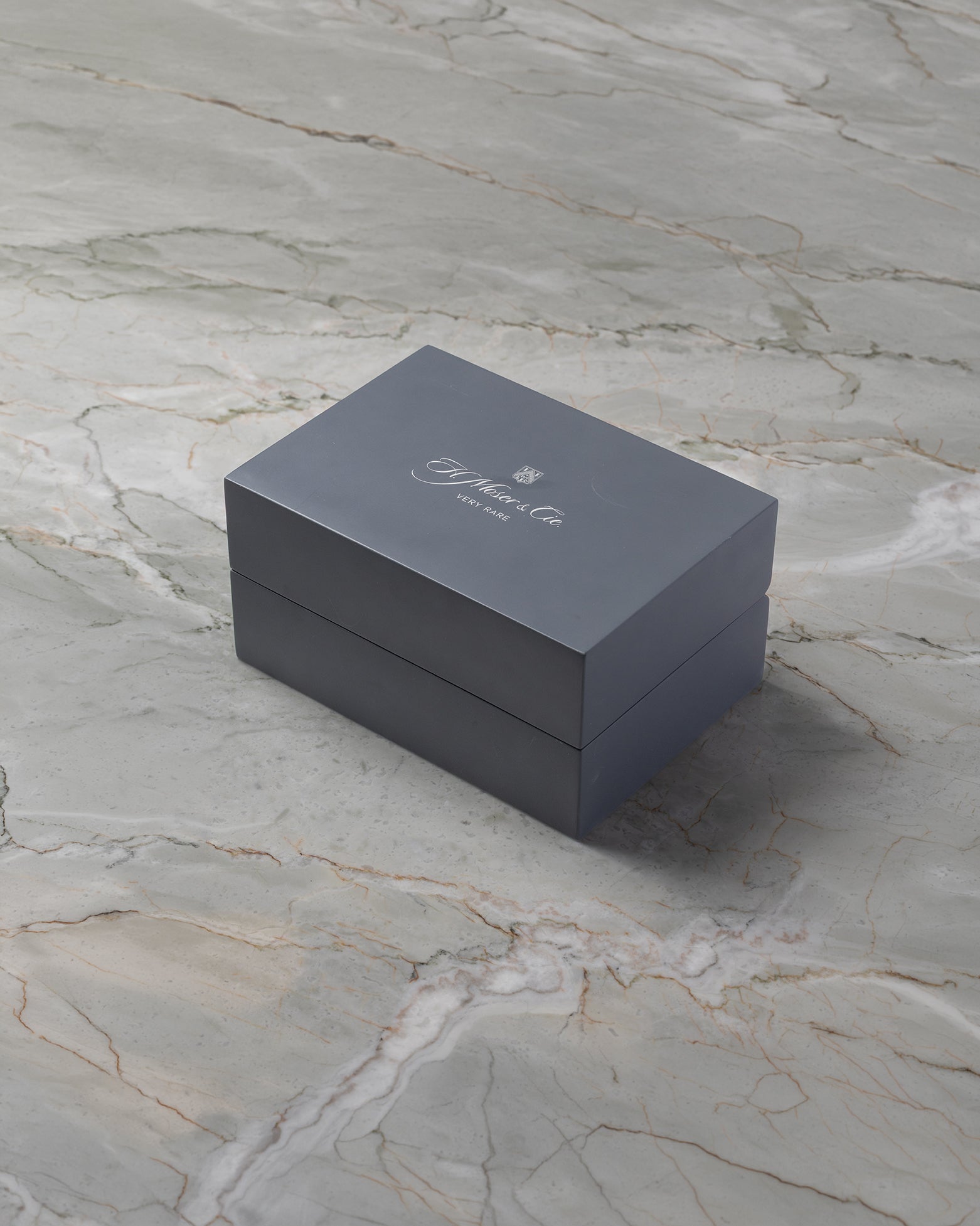 angled overview of the textured slate grey H. Moser & Cie. luxury watch presentation box on a marble surface