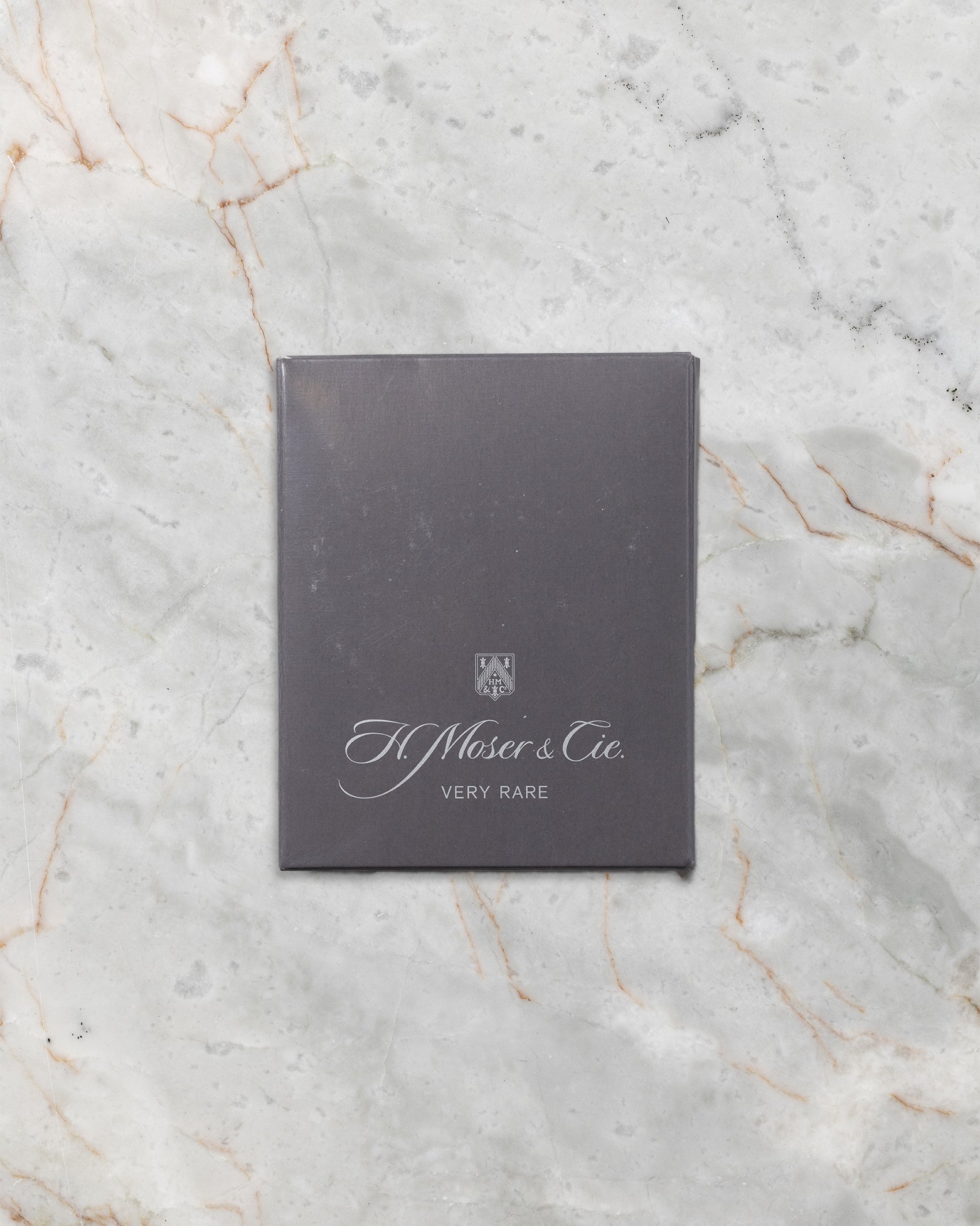 dark charcoal gray H. Moser & Cie. official user manual and instruction booklet displayed flat on marble