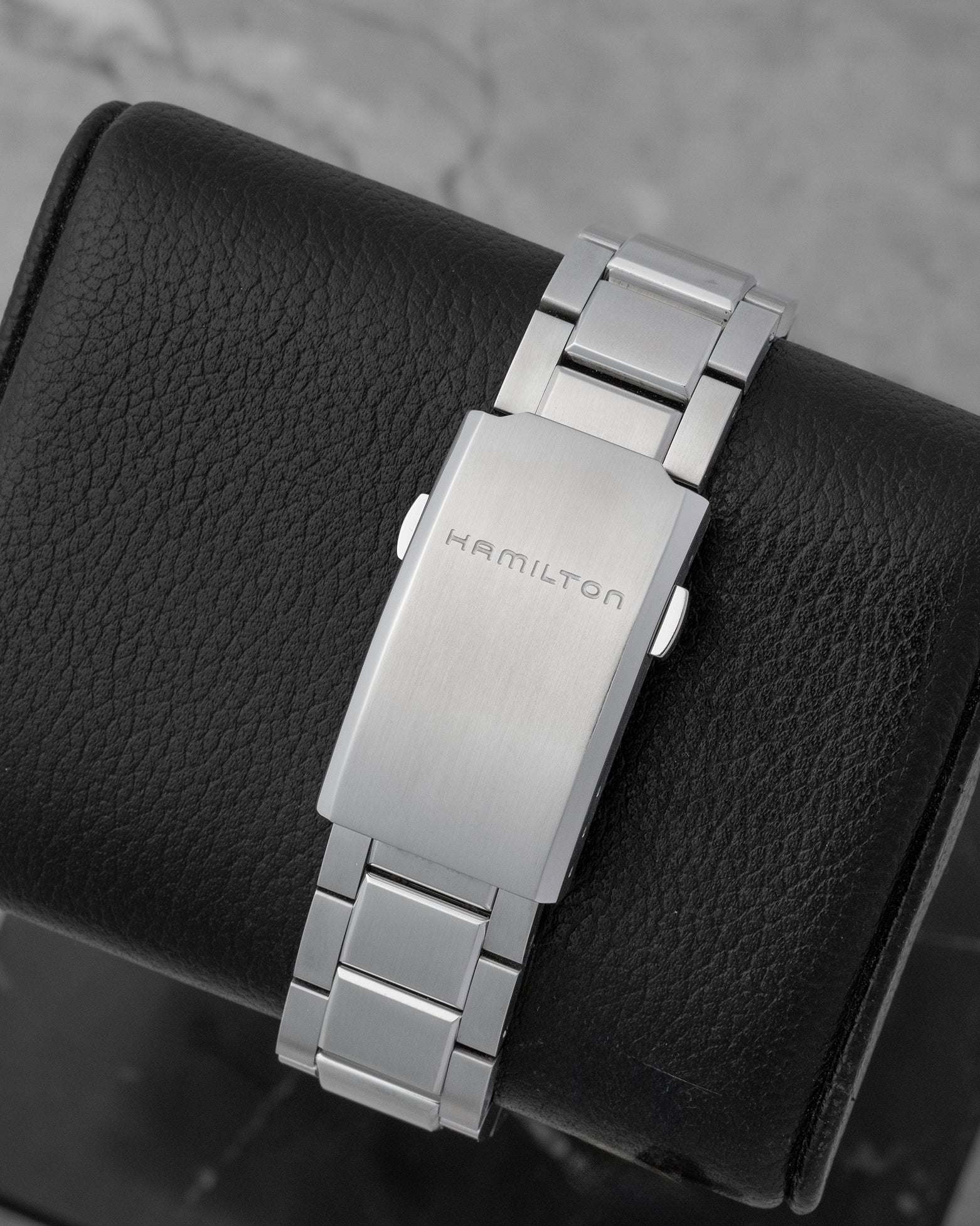 The flat stainless steel folding deployment clasp with an engraved Hamilton logo on a 3-link watch bracelet