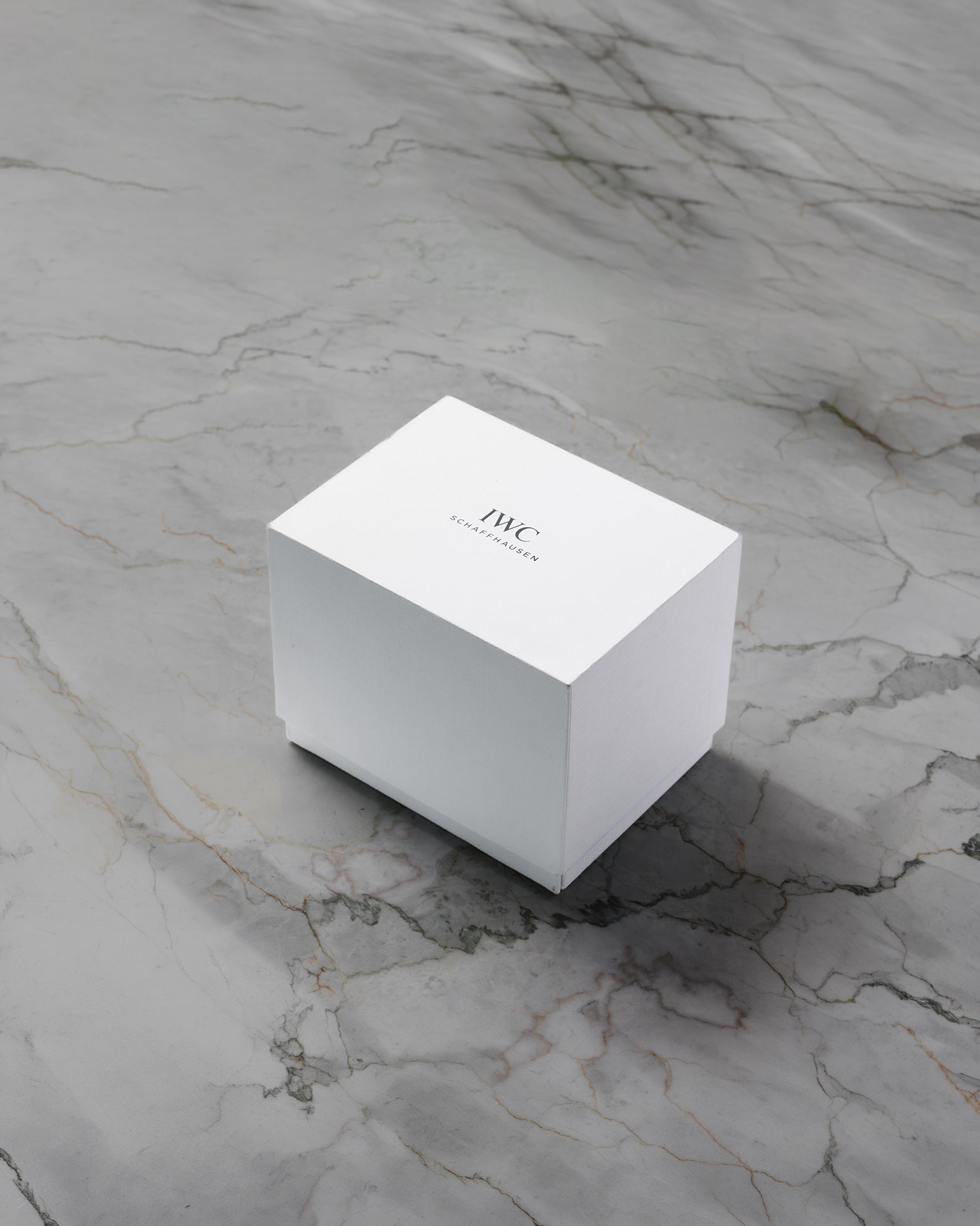 A closed clean white rectangular IWC Schaffhausen luxury watch presentation box sitting centered on a grey marble surface