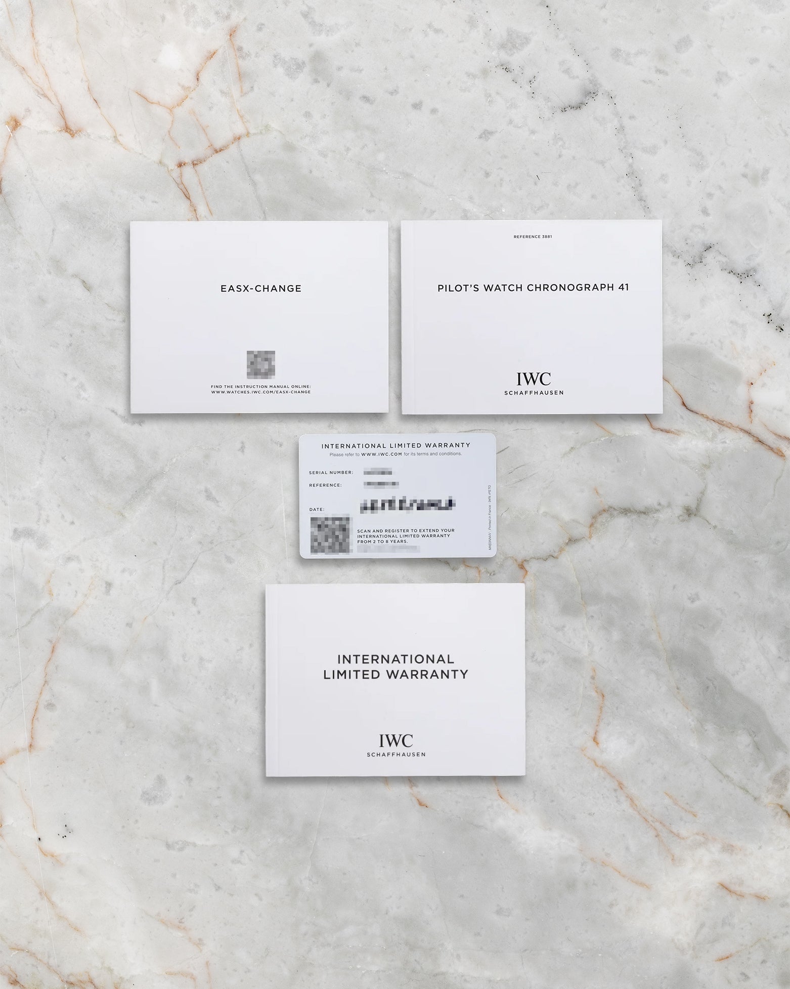 The official IWC international limited warranty card, service manual, and user guide booklets laid flat on a marble background