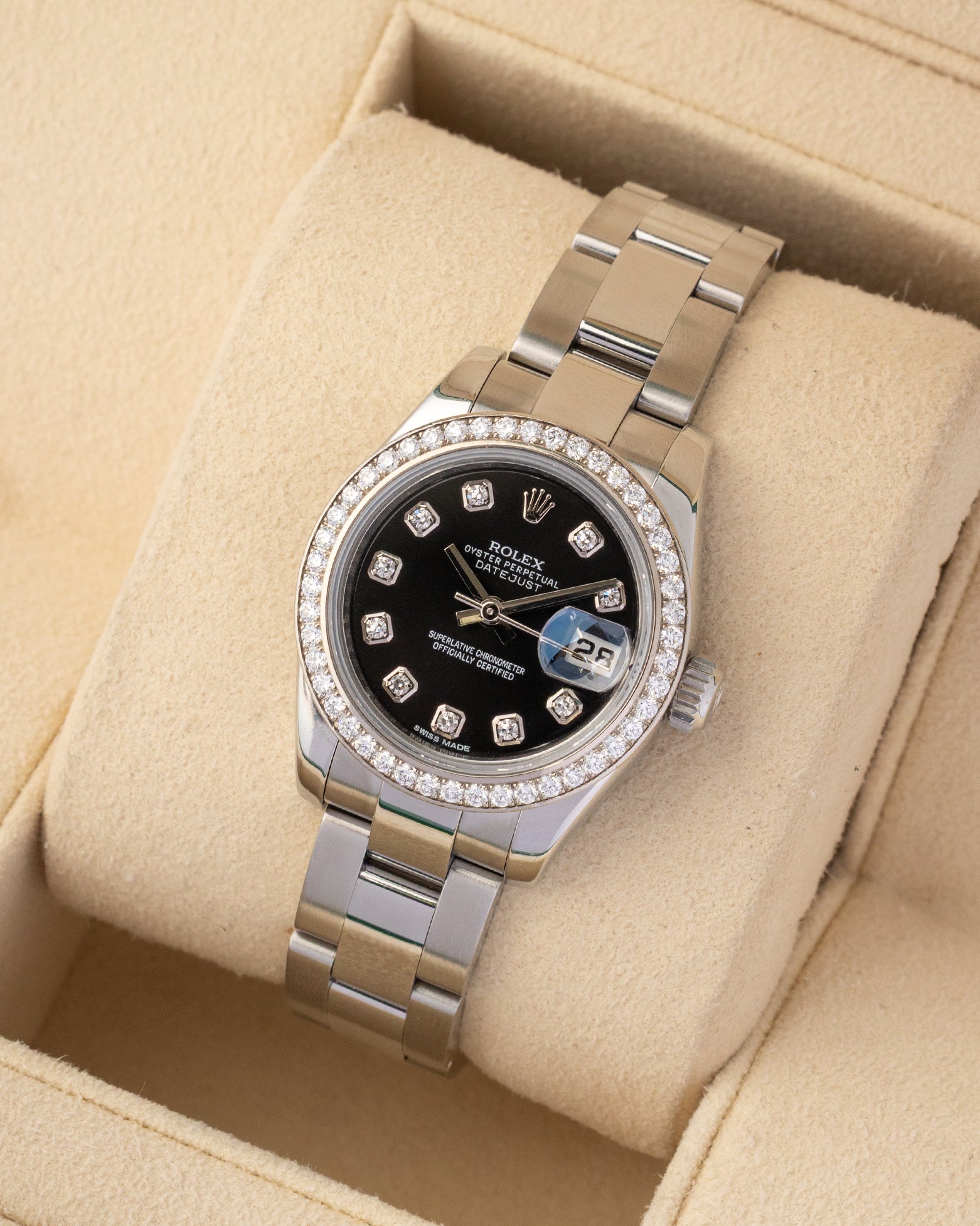 A high-angle three-quarter studio portrait of the 26mm steel watch case displaying the mirror-polished center links of its solid Oystersteel bracelet on a beige cushion