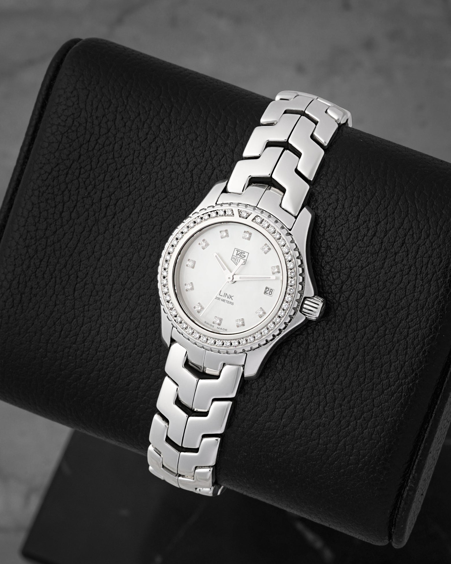 A high-angle three-quarter portrait of the polished 27mm stainless steel watch case resting on a black leather display cushion to emphasize the brilliant-cut diamonds