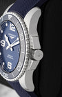 Side profile view showing the protective crown guards, screw-down winding crown, and stainless steel case on blue Longines HydroConquest L3.781.4.96.9
