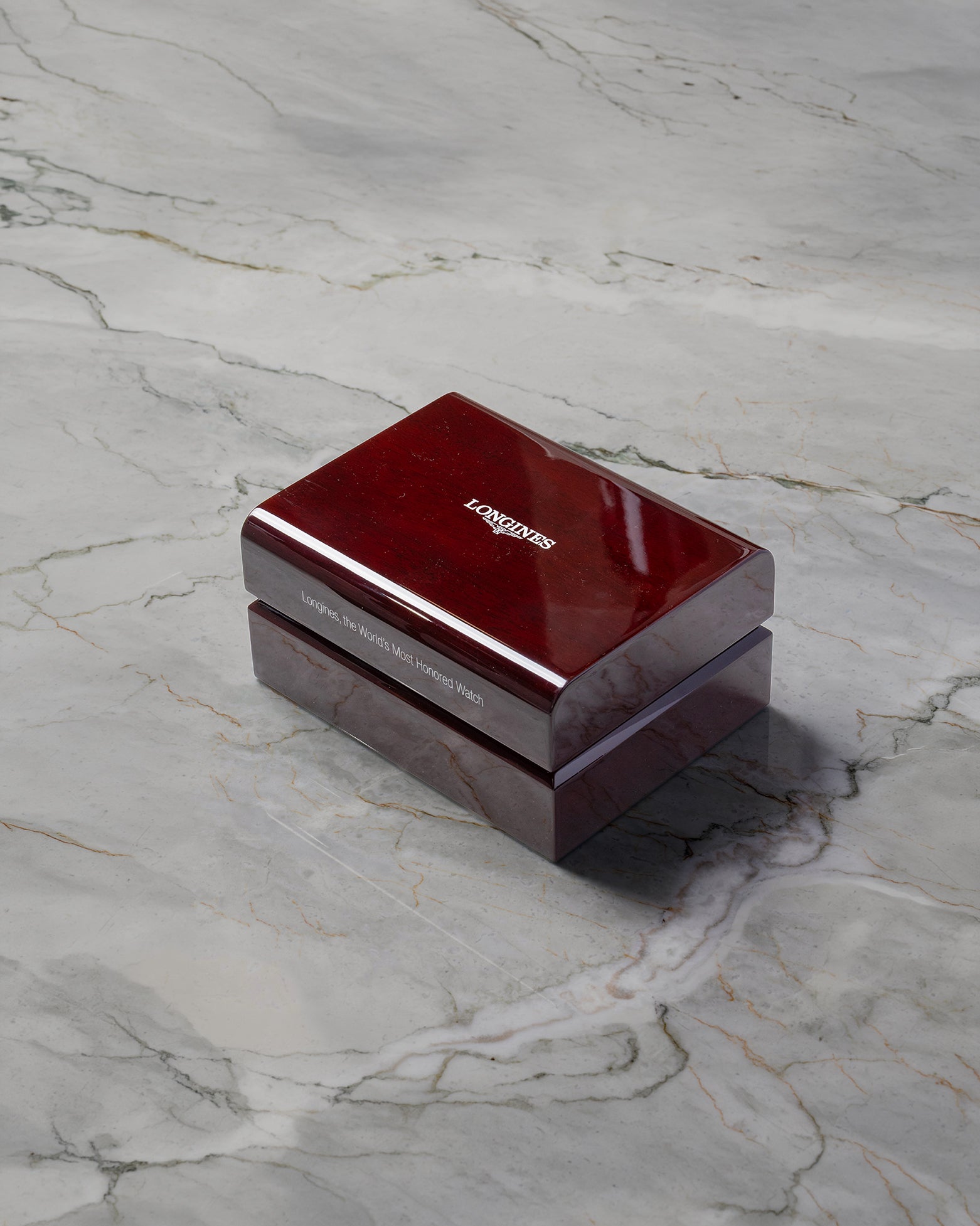 A closed rectangular high-gloss cherry wood finish Longines luxury watch presentation box sitting centered on a grey marble background