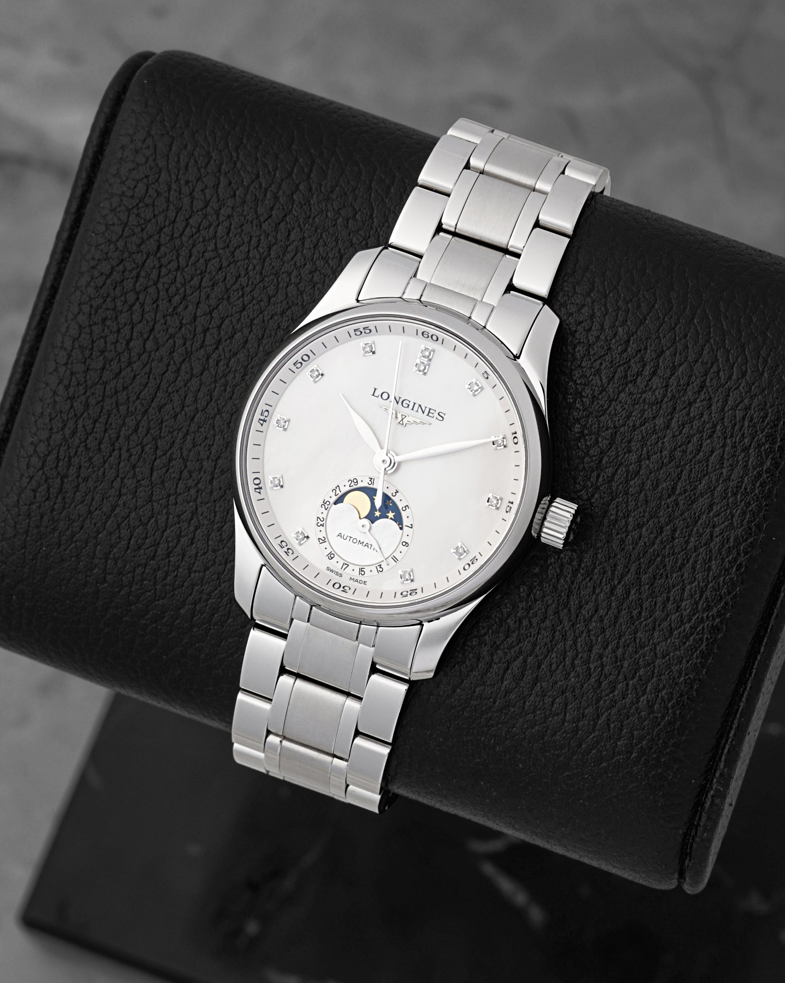 A high-angle three-quarter view of the polished 34mm stainless steel watch case resting on a black leather cushion to highlight the radial date ring encircling the moonphase display