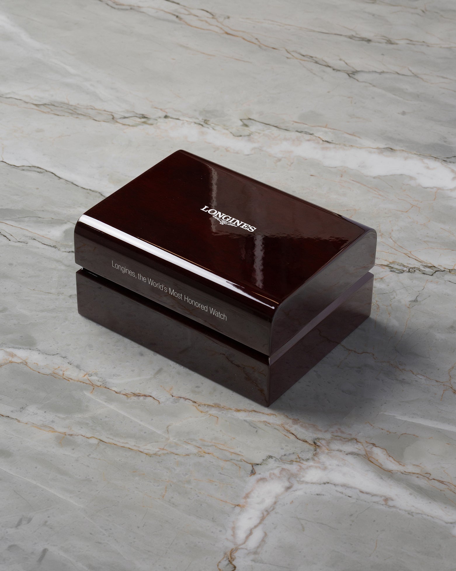 A high-angle three-quarter shot of the official premium dark brown lacquered wood grain watch presentation chest resting closed on a grey marble backdrop