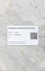 A top-down flat lay view of the official white Montblanc international guarantee card showing the printed reference block and a scannable QR code on a grey marble surface
