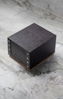 Original square textured dark grey Breitling luxury watch presentation box with stud details displayed on a premium white marble surface