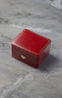 Original square textured red leatherette Cartier luxury watch presentation box featuring gold filigree detailing, displayed on a white marble surface