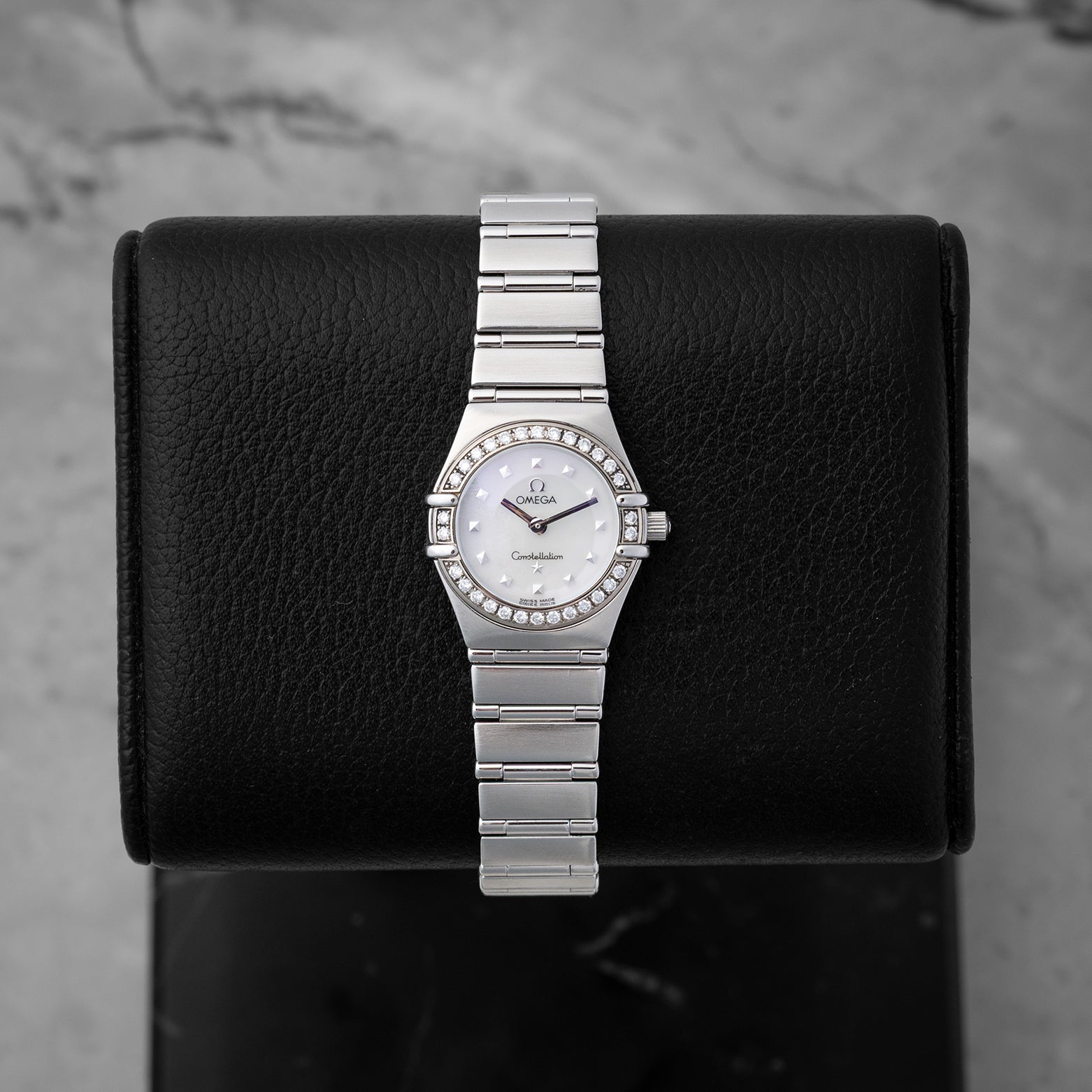 Omega Constellation 1465.71.00 26mm luxury watch in stainless steel, featuring a white mother of pearl dial and factory diamond bezel, displayed on a black cushion.