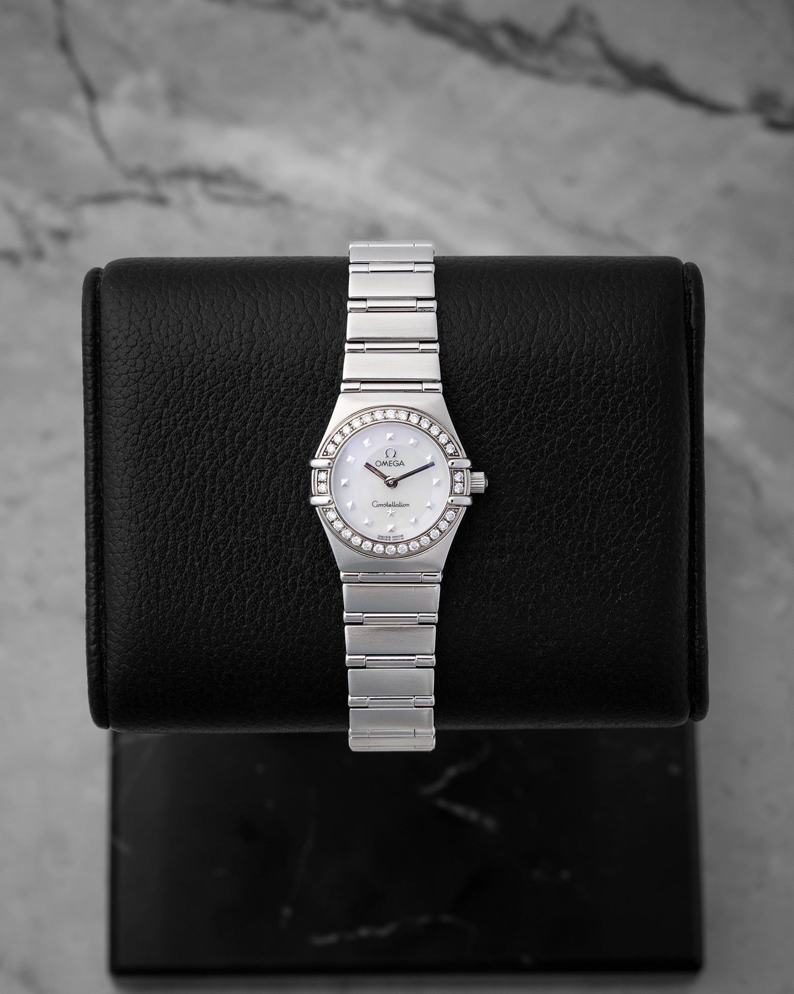 Omega Constellation 1465.71.00 26mm luxury watch in stainless steel, featuring a white mother of pearl dial and factory diamond bezel, displayed on a black cushion.