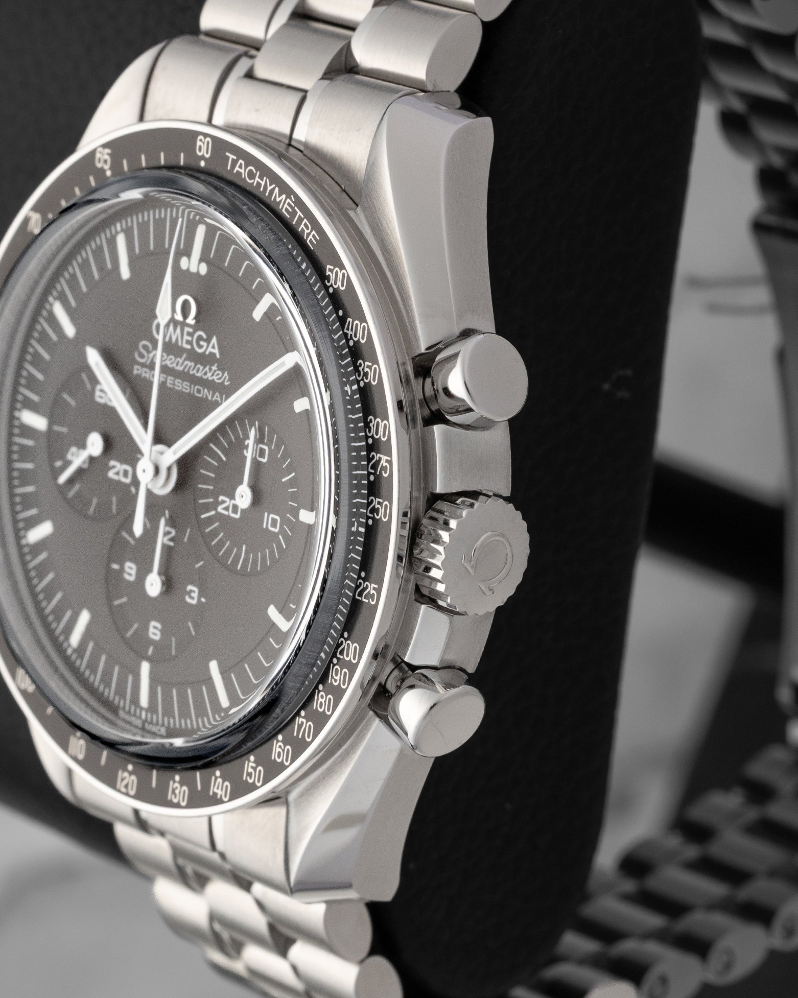 Close-up right profile view of the watch head highlighting the polished piston chronograph pushers flanking the fluted winding crown embossed with the Omega logo