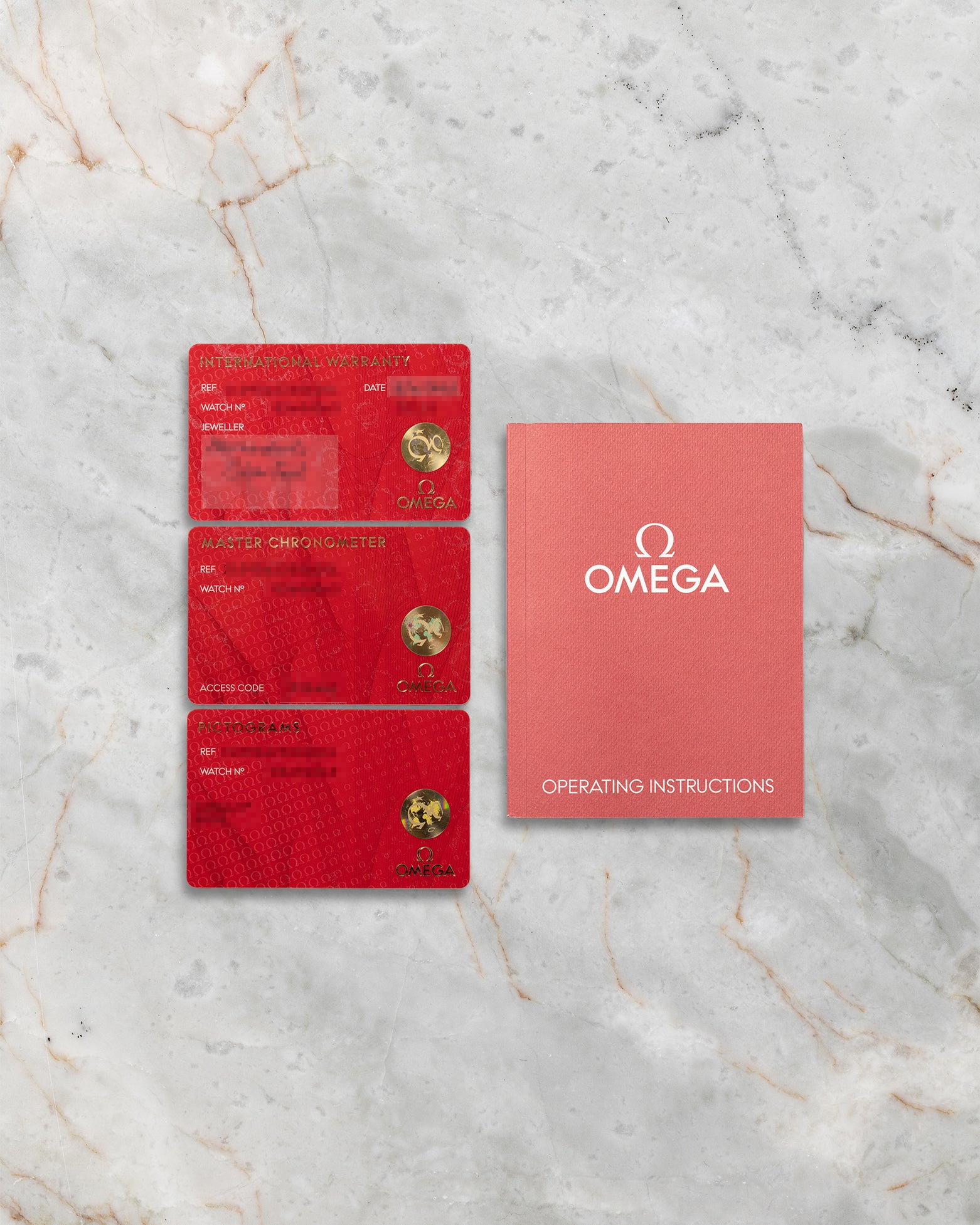 The official red Omega pictogram, master chronometer, and international warranty cards alongside the user instruction guide at Noahs Fine Watches and Jewelry Dallas