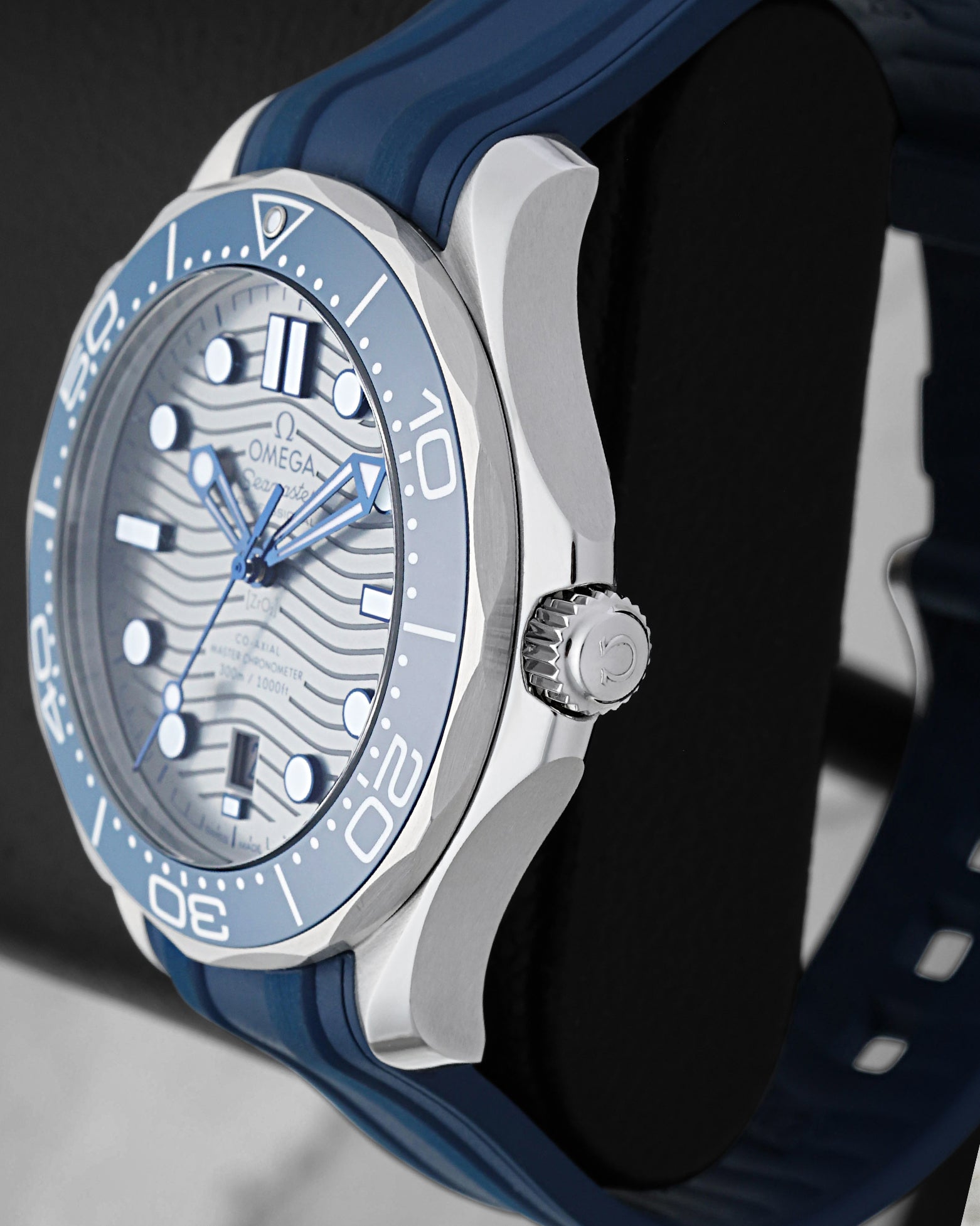 Right side profile view highlighting the stainless steel case finish, screw-down crown, and blue ceramic unidirectional rotating bezel of an Omega Seamaster Diver 300M