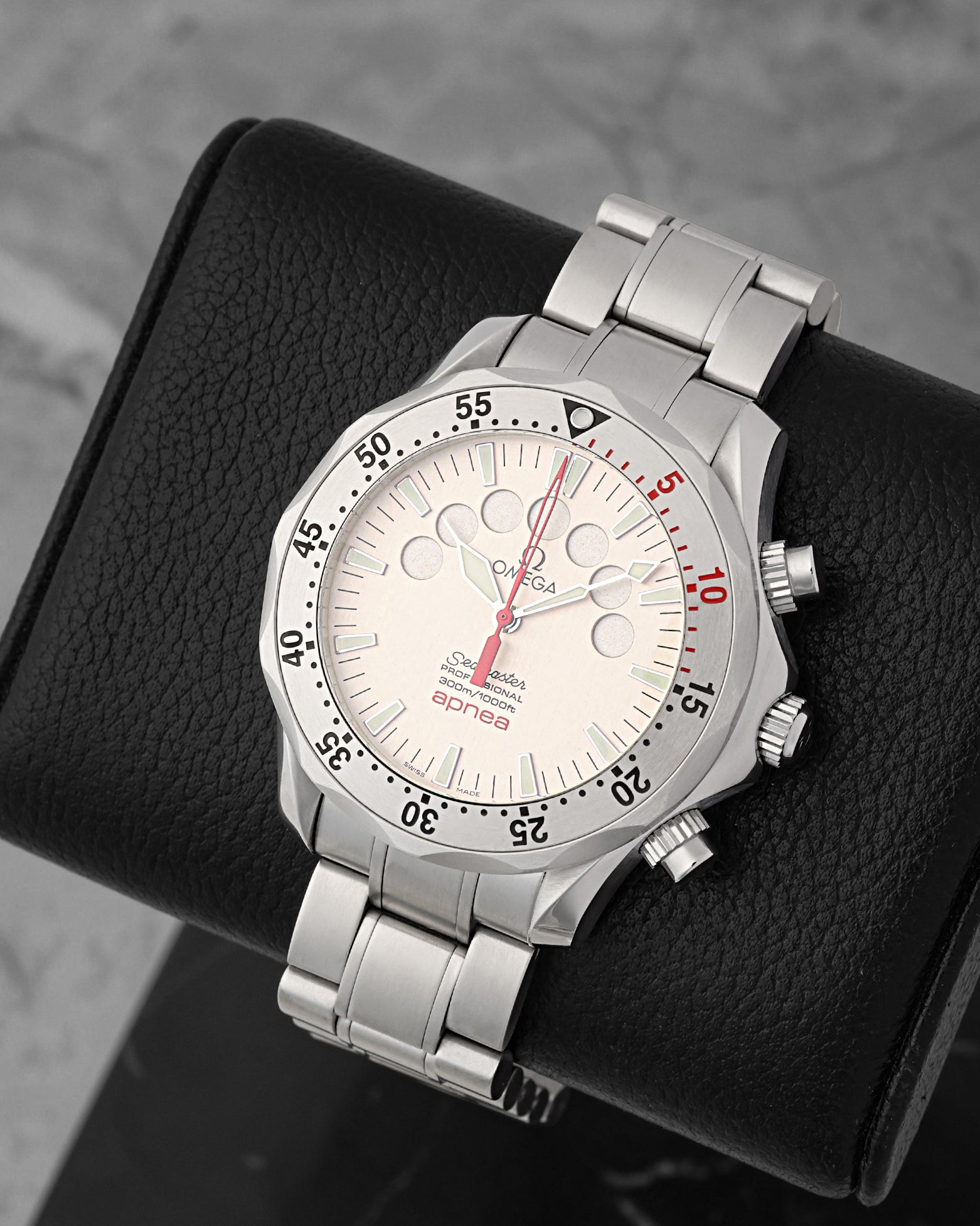 A high-angle three-quarter studio portrait of the 41.5mm Omega Seamaster Apnea case showcasing its distinct unidirectional rotating bezel with a red 10-minute scale segment