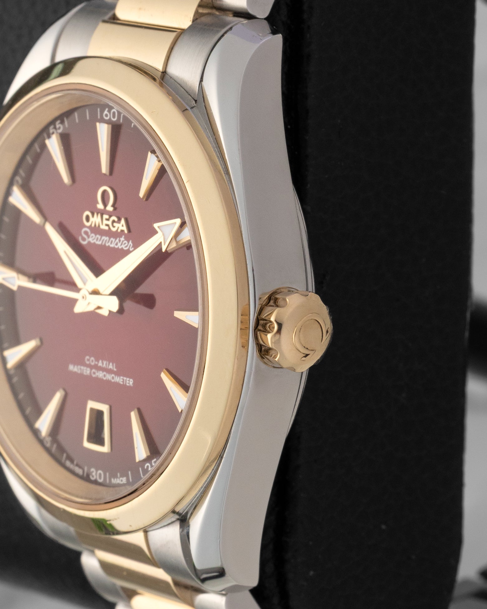 Close-up right profile view of the watch head focusing on the polished 18k Moonshine gold bezel ring and the conical screw-in winding crown embossed with the Omega logo