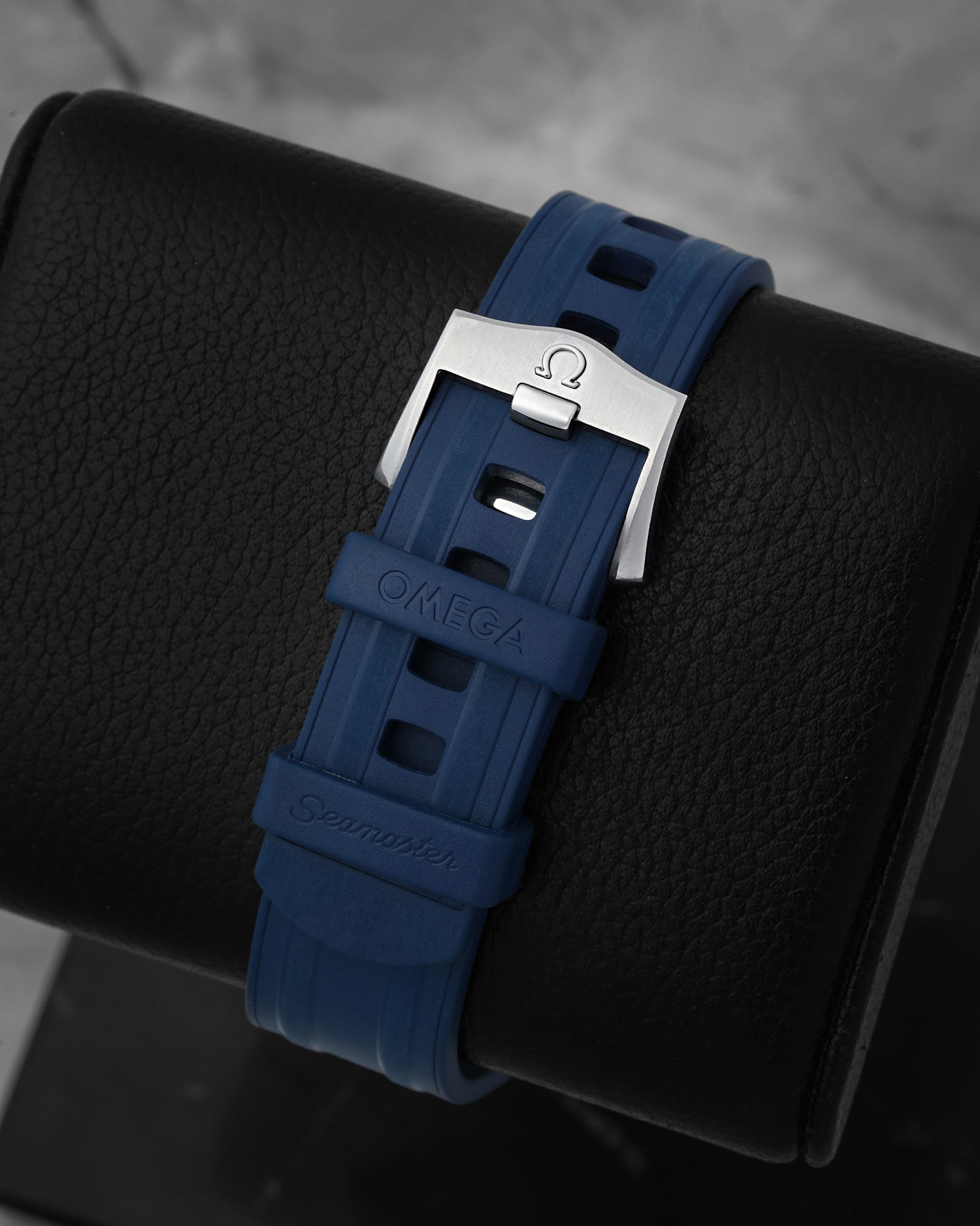 Close-up of the integrated blue structured rubber watch strap and engraved stainless steel pin tang buckle for an Omega Seamaster