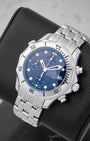 An angled studio shot of a stainless steel neo-vintage Omega Seamaster 300M Chronograph resting on a leather cushion
