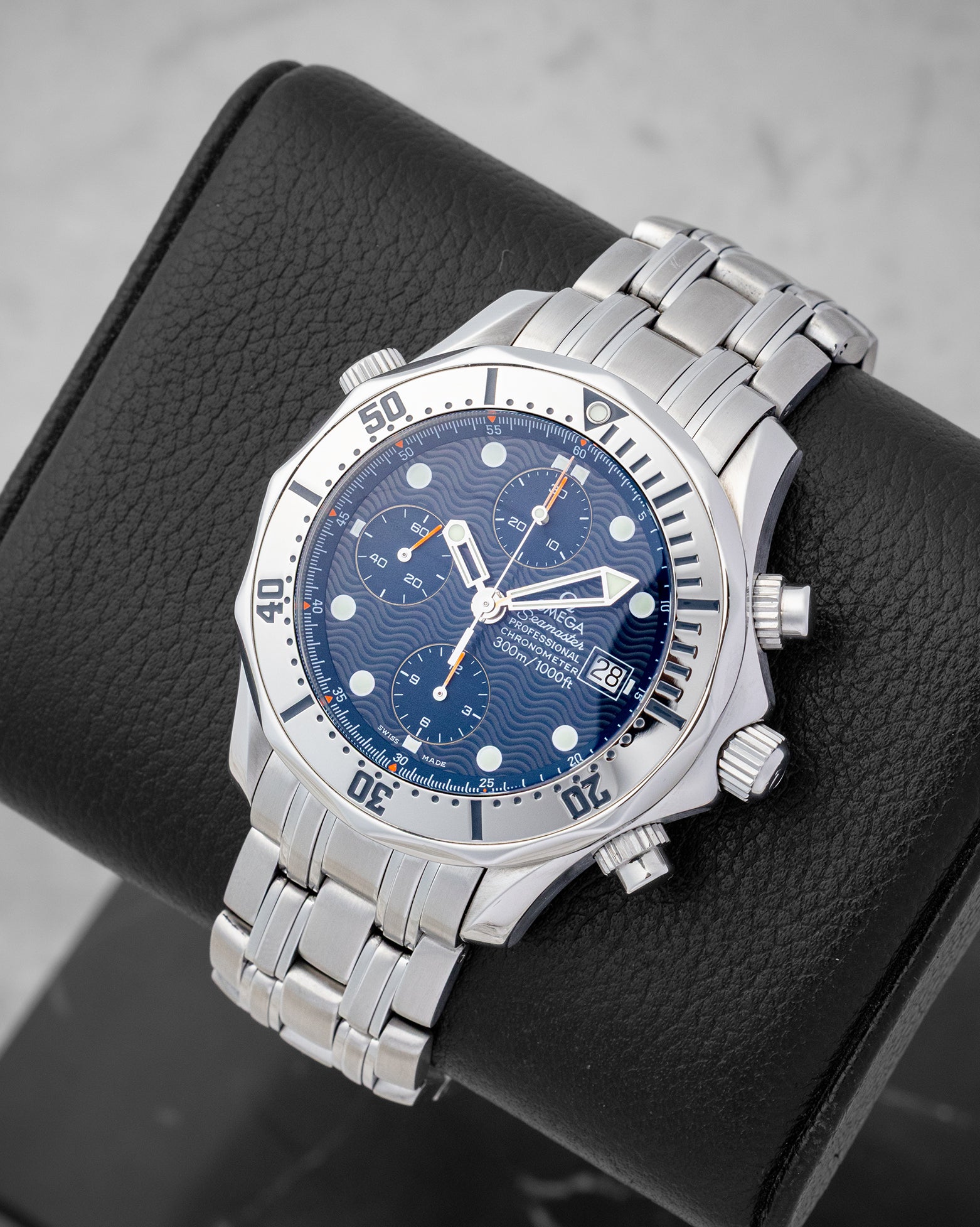 An angled studio shot of a stainless steel neo-vintage Omega Seamaster 300M Chronograph resting on a leather cushion