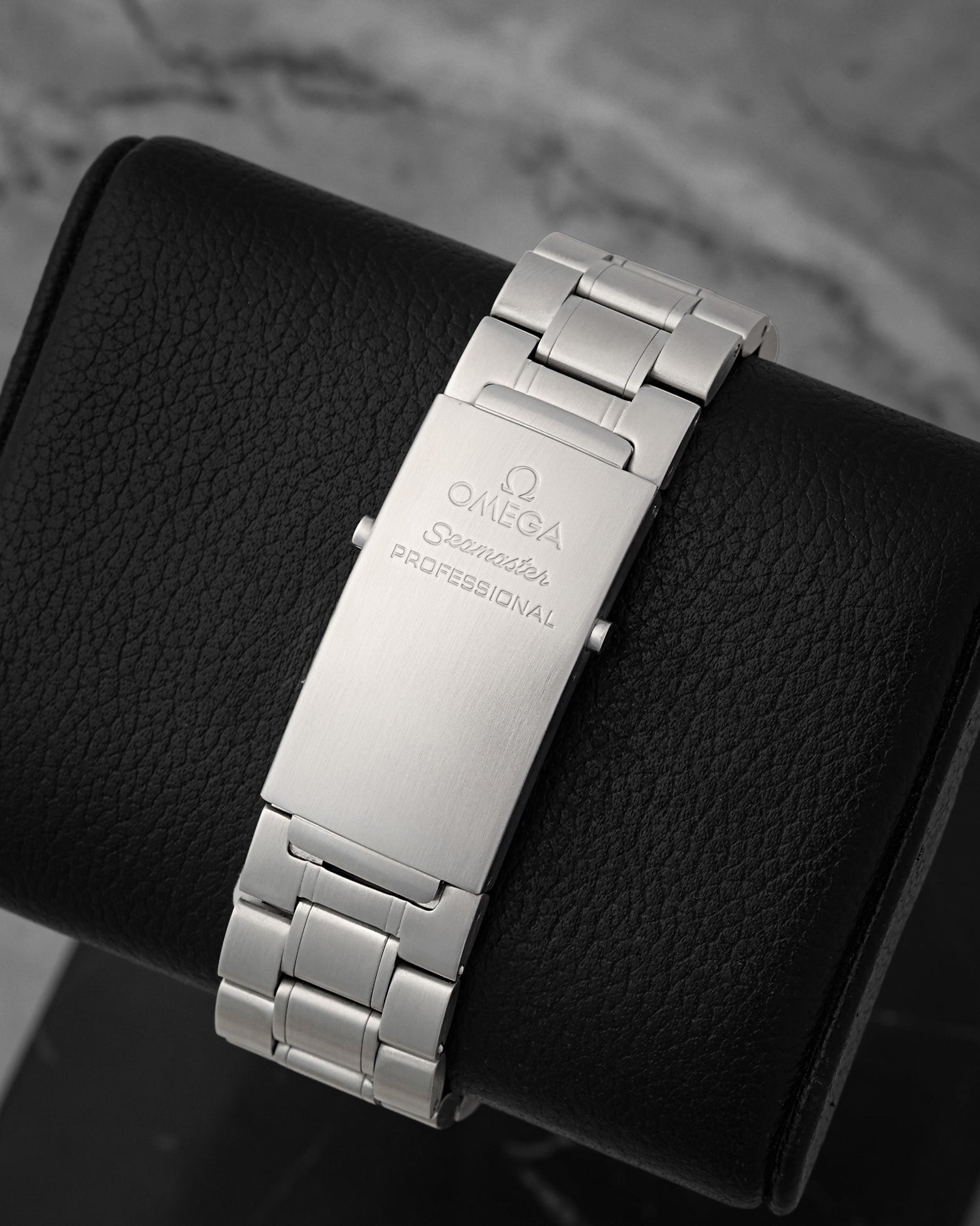 A rear view of the satin-finished three-link stainless steel bracelet focusing on the classic fold-over professional deployment clasp engraved with the Omega Seamaster speedmaster emblem text