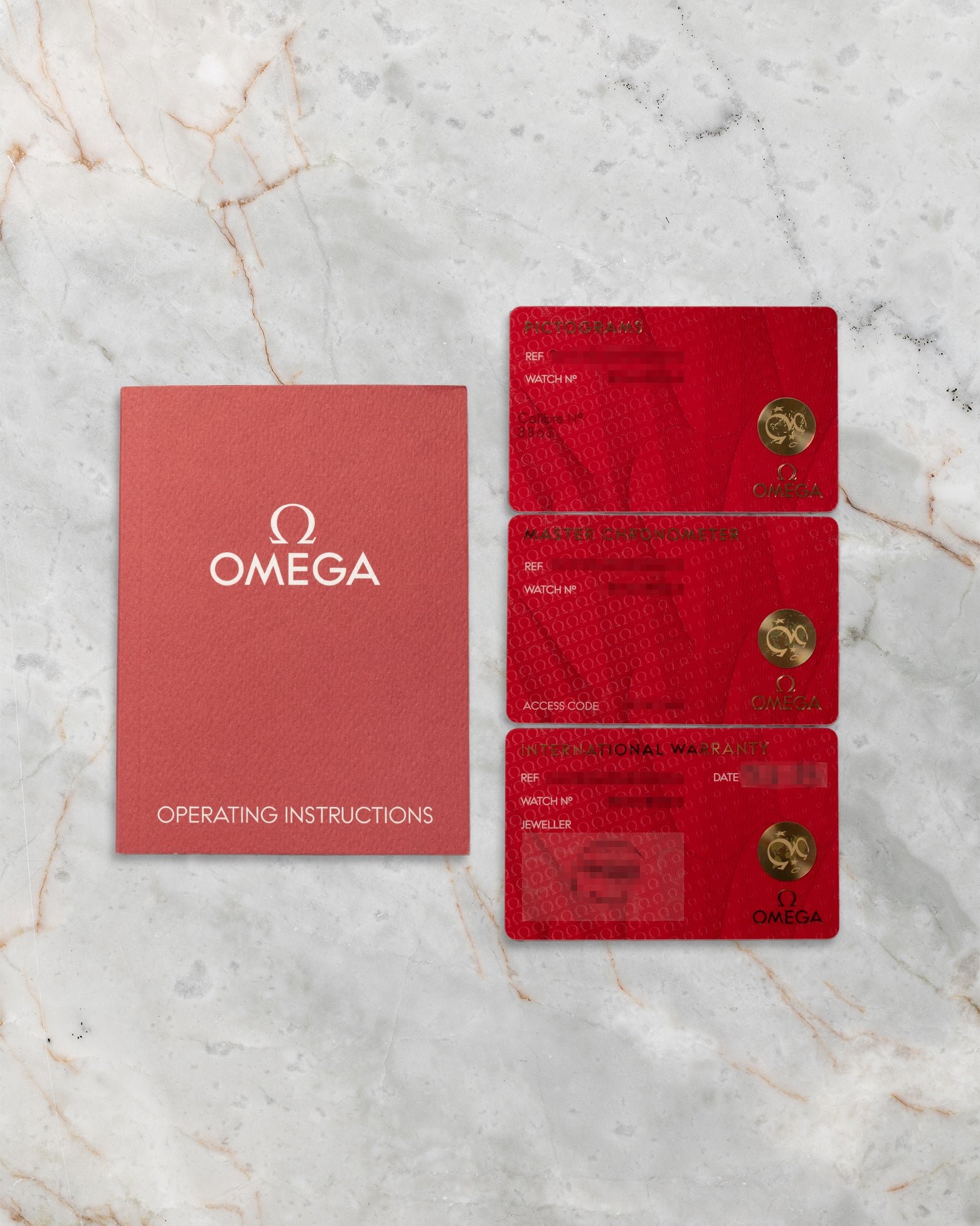 A top-down flat lay view of the official red Omega user operating manual alongside the triple red cards including the international warranty, pictogram, and master chronometer certification